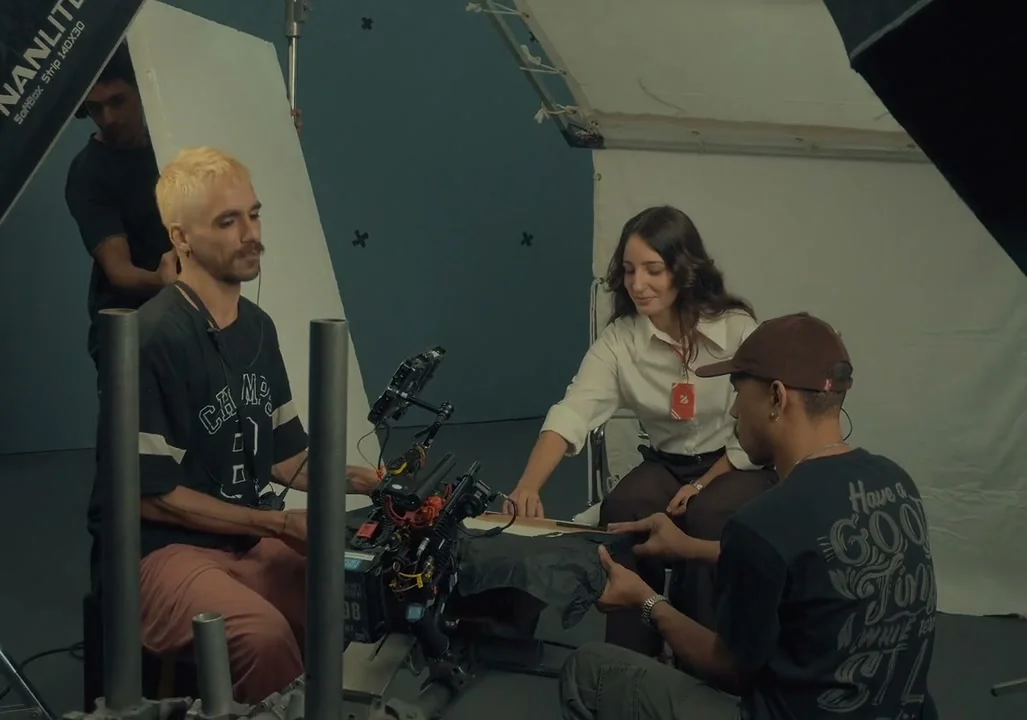 Equipe prepara a câmera diante da atriz sentada à mesa do escritório.
